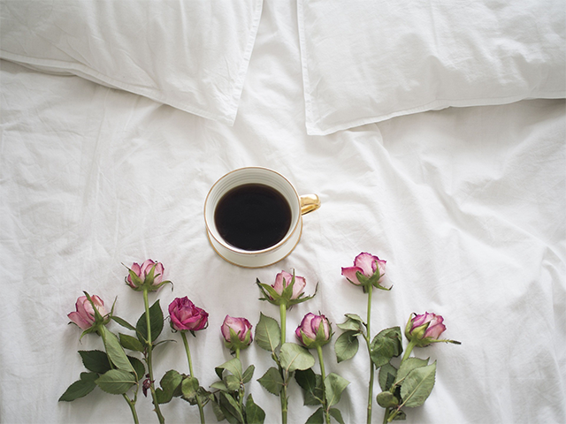 ベッドの上にコーヒーと花があるイメージ。無理をしないように過ごそうと心がけている。