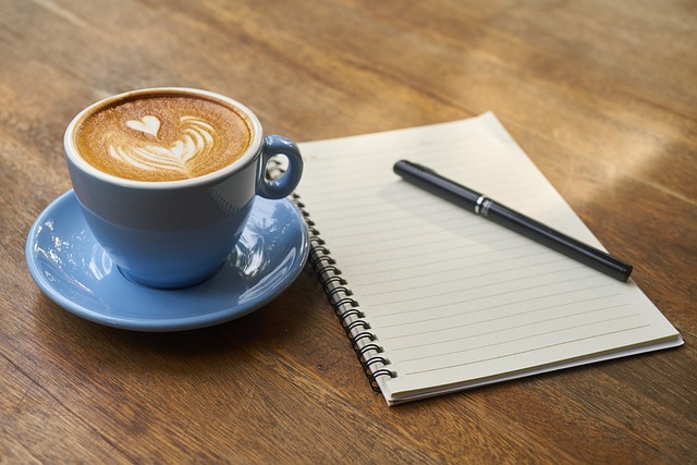 コーヒーとノートとペンが置かれているイメージ
