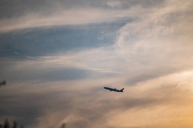 夕暮れの空を飛ぶ飛行機のシルエット。雲と柔らかな光が広がる空。