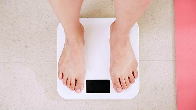 白い体重計に乗る裸足の人の足。線維筋痛症と体重増加の関係について説明しています。