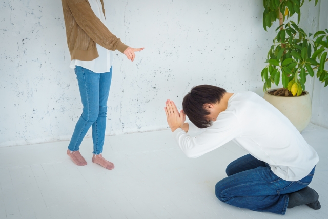 床にひざまずいて謝る男性と立って指を指す女性。