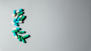 灰色の背景に並べられた緑と白の錠剤とカプセル。