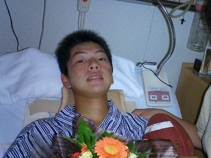 病院のベッドに横たわり、花束を持つ男性。