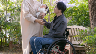 公園で赤ちゃんを抱いている人と車椅子に座っている人が一緒にいる写真。車椅子に関する質問を子どもに説明している様子。