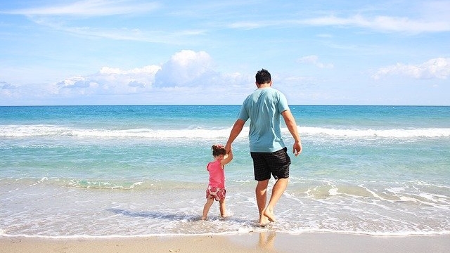 ビーチで一緒に海に向かって歩く父親と子供の後ろ姿。