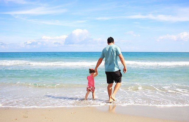 ビーチで一緒に海に向かって歩く父親と子供の後ろ姿。