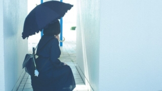 白い通路で黒い日傘を差して座っている少女