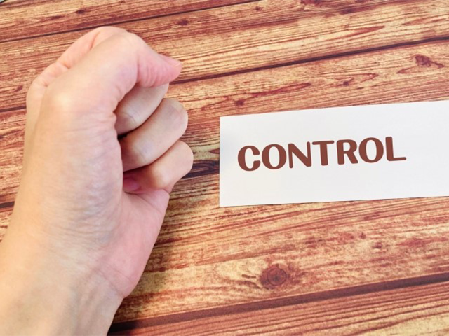 木製のテーブルに「CONTROL」と書かれたカードと、その上で握りこぶしを作っている手。メンタルヘルスを守るためにコントロールを手放すことの象徴。