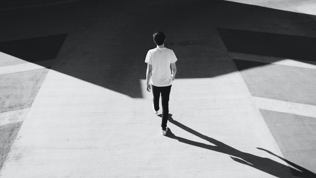 橋の下を歩く男性の後ろ姿、光と影のコントラストが印象的な白黒写真