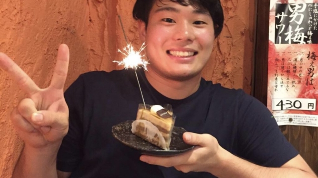 ケーキと花火を持って笑顔でピースサインをする男性。