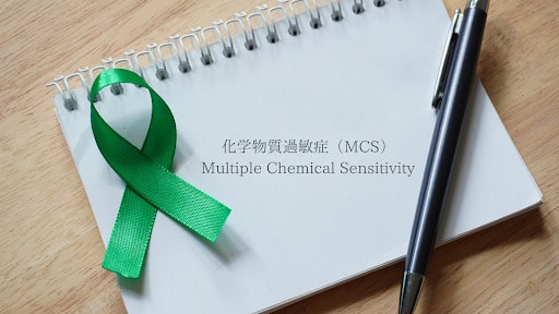 緑のリボンとペンが置かれたノート。化学物質過敏症（MCS）の啓発を象徴しています。