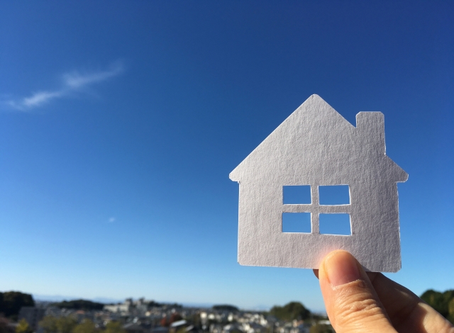 青空を背景に紙で作られた家のシルエットを持つ手の画像。