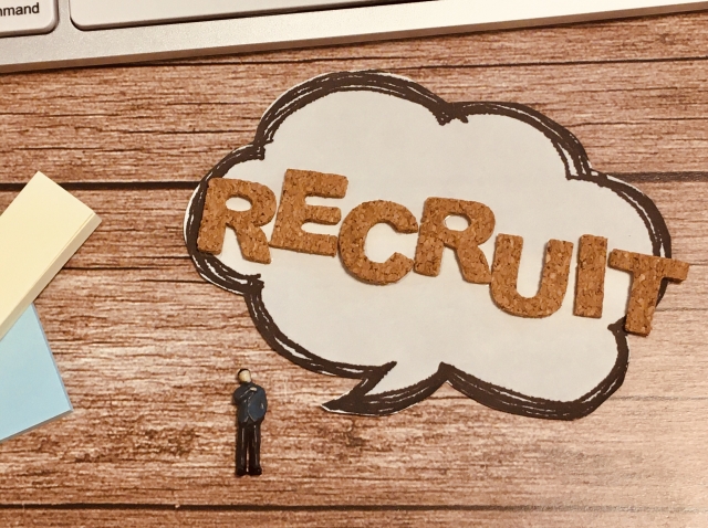  「RECRUIT」と書かれたコルク素材の文字が描かれた吹き出しと、小さな人物フィギュアがデスク上に置かれている。障害者雇用の面接に関連するコンセプトを示す画像。