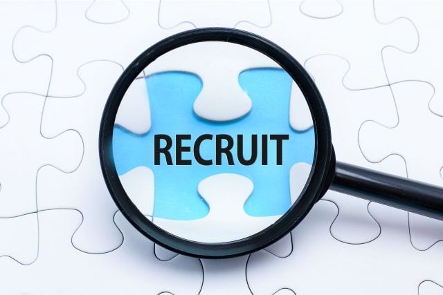 拡大鏡で「RECRUIT」と書かれたパズルのピースを拡大している画像。障がい者の就職フェスに関連する企業のニーズを示唆。