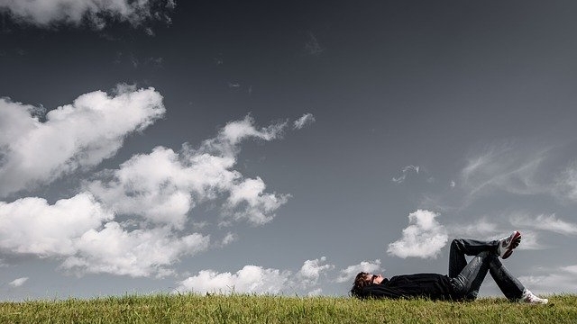 曇り空の下、草の上に寝転んでリラックスしている人。