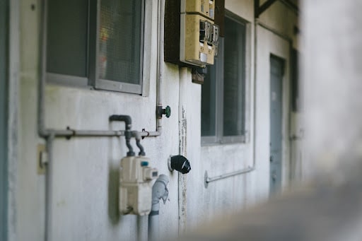 古い建物の外壁に設置されたメーターや配管。21歳で生活保護を受給する20代の難病患者が直面する生活困窮とセーフティネットについて示す画像。