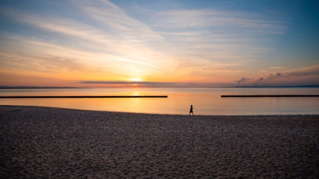 夕日が沈むビーチを一人で歩く人のシルエット。静かな海と広がる砂浜。