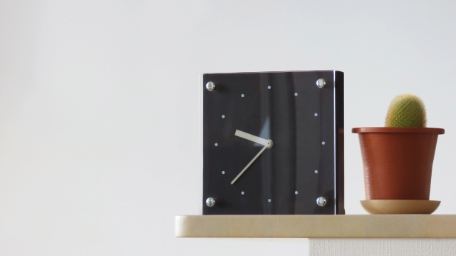 シンプルなデザインの時計とサボテンの鉢植えが置かれた棚。マルチタスクとADHDの時間管理の課題を示す画像。