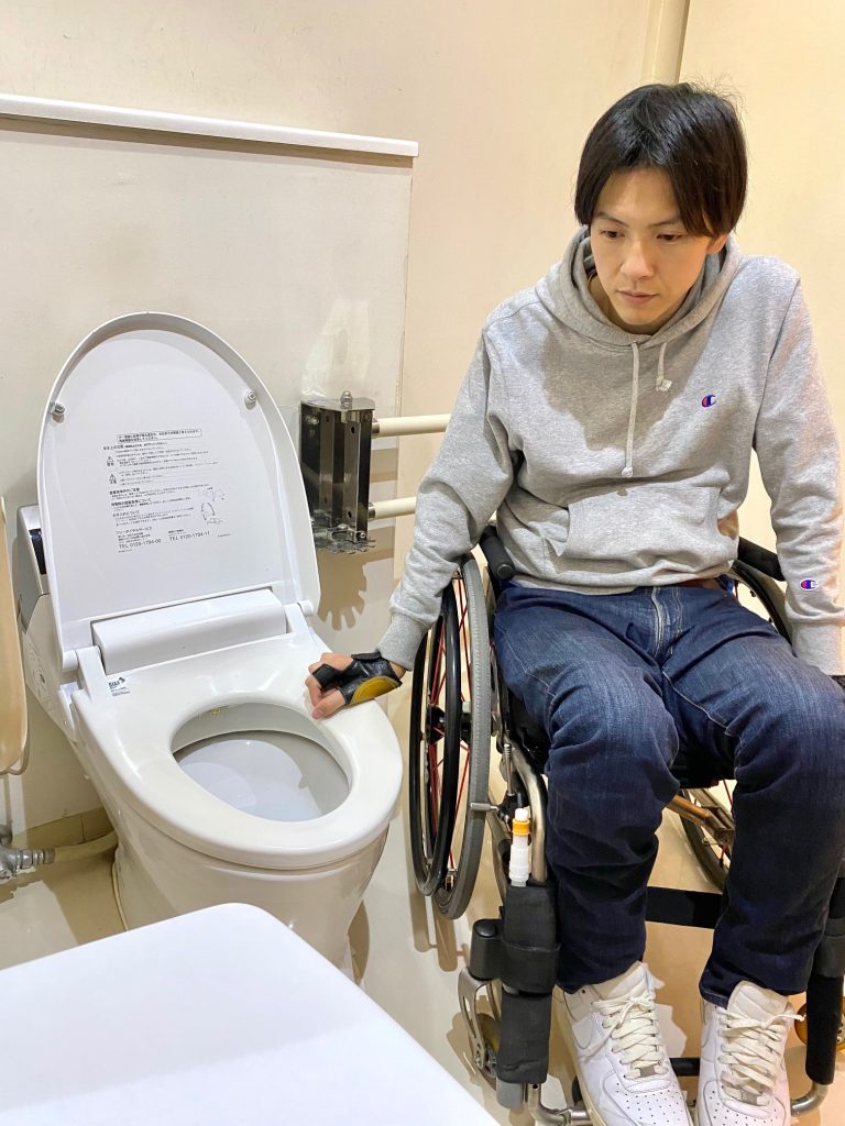 車いすに座っている男性がバリアフリーのトイレを使用しようとしている様子。職場環境におけるアクセシビリティの問題を示しています。