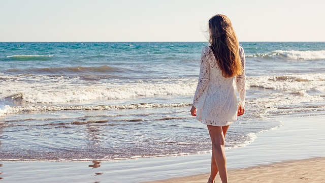白いレースのワンピースを着て、海辺を歩く女性。