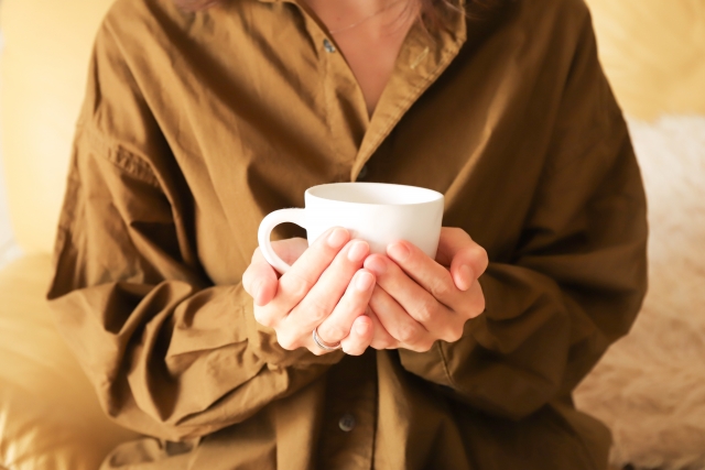 コーヒーマグを持つ茶色のシャツを着た女性の手元