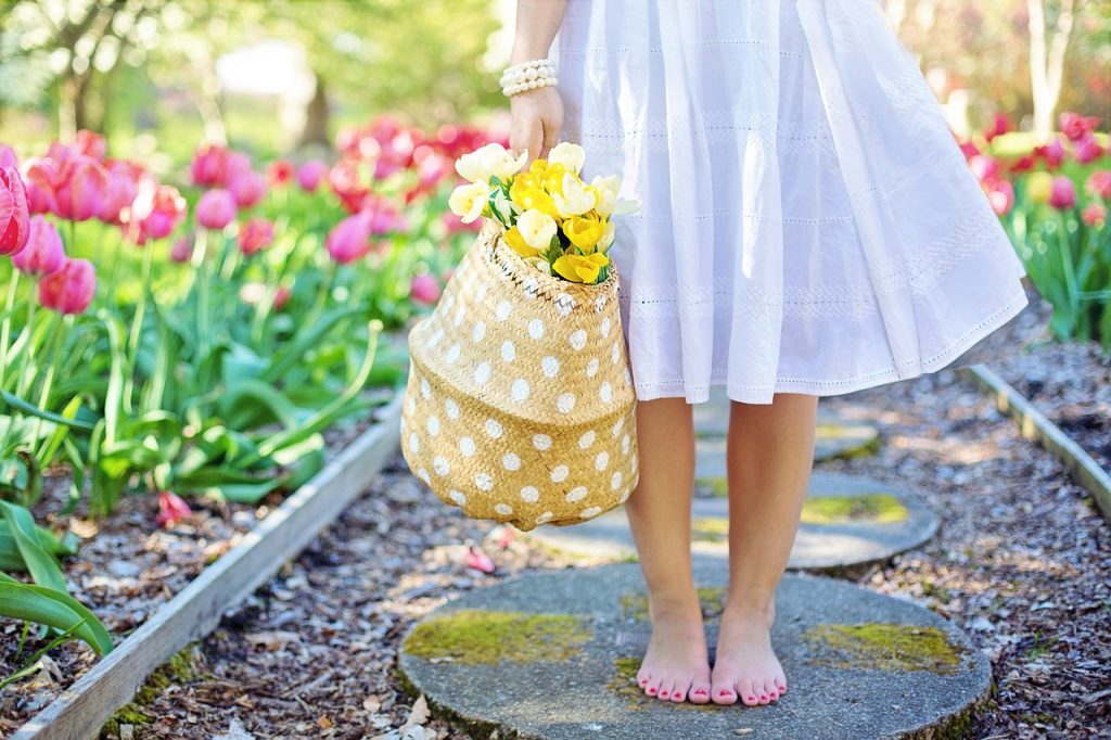 裸足で庭の小道を歩き、花が入ったバスケットを持つ女性。HSPとうつ病に関する記事で、自然との触れ合いやリラックスの重要性を示す画像。