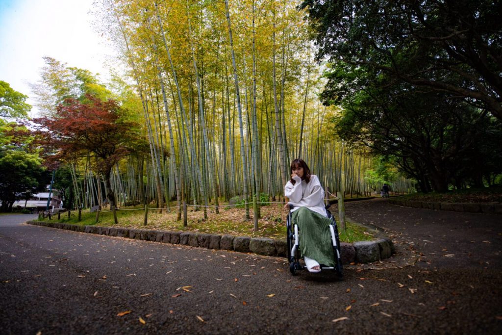 車椅子に座った女性が竹林の中の道端にいる様子。