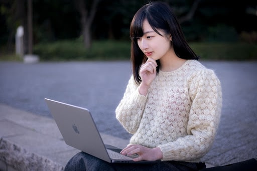 公園でノートパソコンを使っているセーターを着た女性