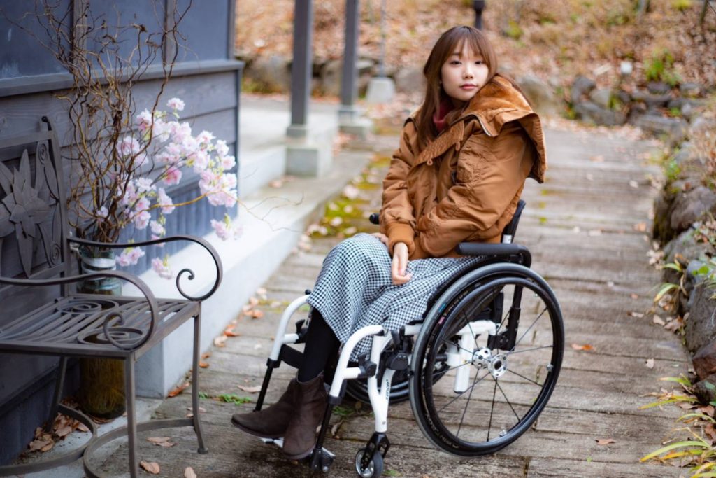 寒い時期に撮られた車椅子姿の豆塚さんとピンクの花のイメージ