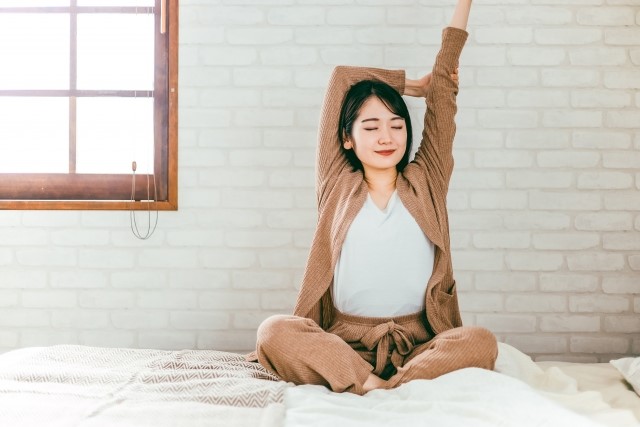 ベッドの上で伸びをする女性の朝の様子。