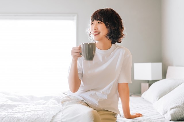 ベッドの上でコーヒーを飲む笑顔の女性。