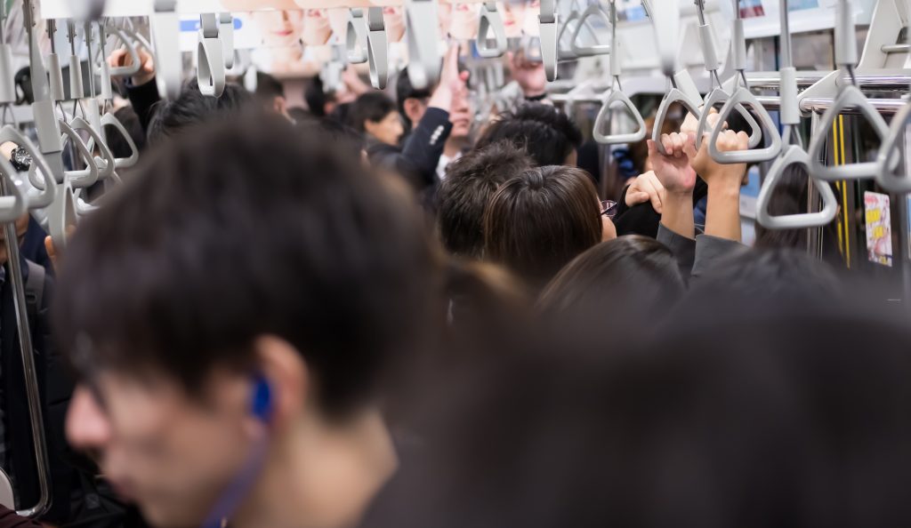 満員の日本の通勤電車の内部の様子。多くの乗客が吊り革に掴まっている。